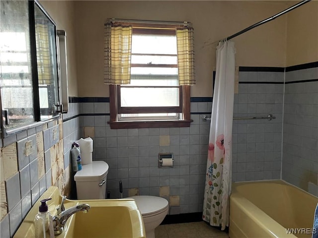 bathroom with plenty of natural light, tile walls, toilet, a wainscoted wall, and tile patterned floors