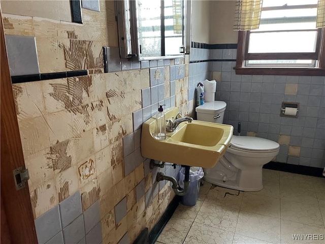 bathroom featuring plenty of natural light, toilet, tile walls, wainscoting, and a sink
