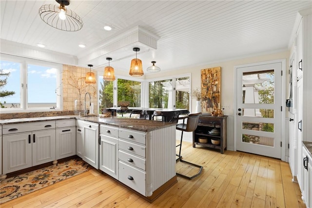 kitchen featuring a breakfast bar, a sink, a peninsula, light wood finished floors, and healthy amount of natural light