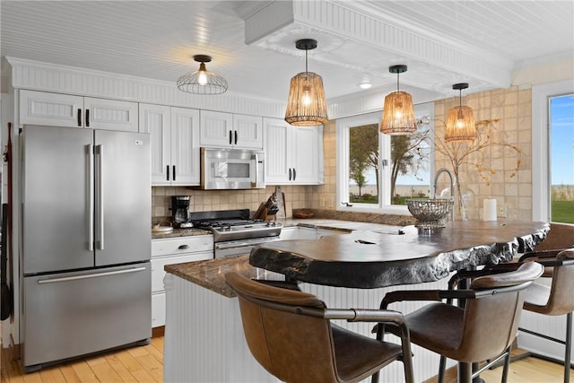kitchen featuring stainless steel appliances, light wood-style flooring, a peninsula, a kitchen bar, and ornamental molding