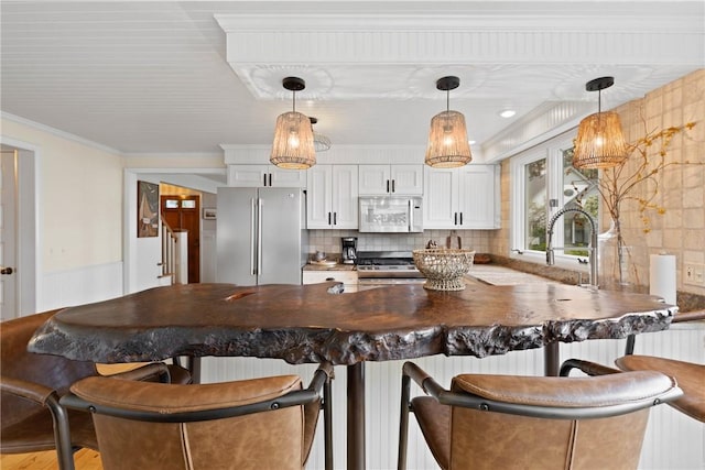 kitchen featuring appliances with stainless steel finishes, white cabinets, a breakfast bar area, decorative backsplash, and ornamental molding