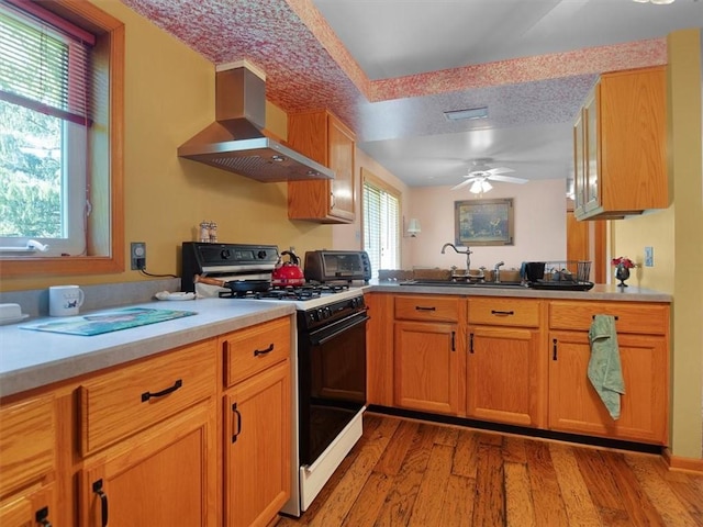 kitchen with gas stove, extractor fan, a sink, light wood-type flooring, and a ceiling fan
