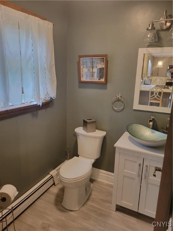 3130 Meadow View Ln, Sennett, NY 13021 - half bathroom featuring baseboard heating, wood finished floors, vanity, toilet, and baseboards