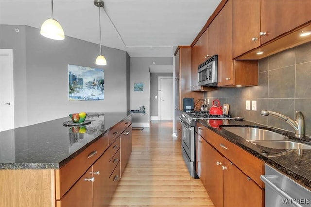 kitchen with appliances with stainless steel finishes, a sink, light wood-type flooring, brown cabinets, and baseboards
