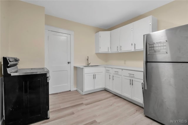 kitchen with freestanding refrigerator, electric range oven, a sink, and light wood finished floors