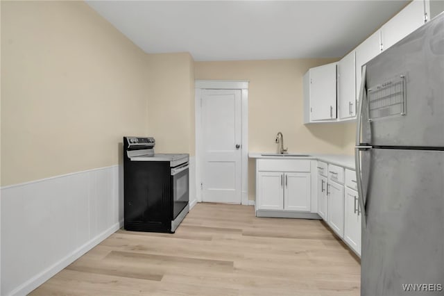 kitchen featuring appliances with stainless steel finishes, a sink, light countertops, white cabinets, and wainscoting