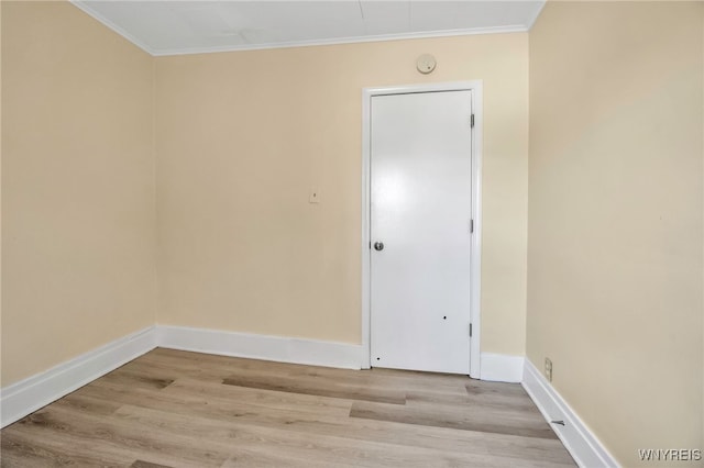 spare room with crown molding, light wood-style floors, and baseboards