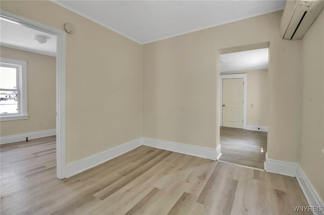 spare room with an AC wall unit, light wood-style floors, crown molding, and baseboards