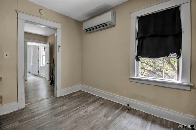 empty room featuring a wall mounted air conditioner, wood finished floors, baseboards, and a smoke detector