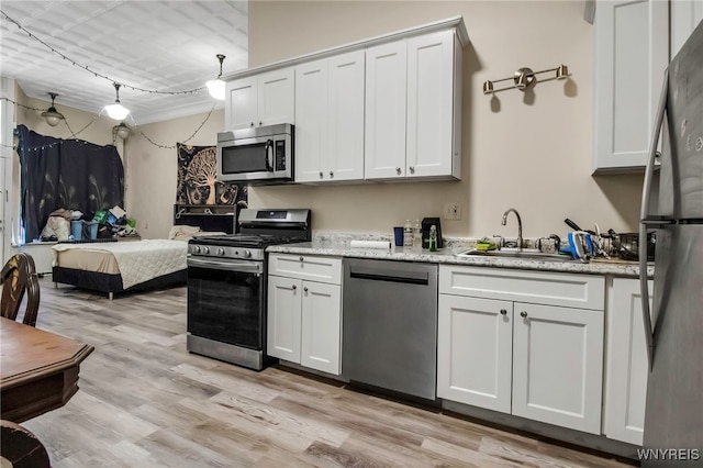 kitchen with stainless steel appliances, a sink, light wood-style flooring, white cabinets, and light stone countertops