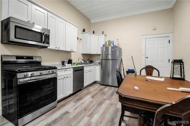 kitchen featuring appliances with stainless steel finishes, light wood-type flooring, a sink, light countertops, and white cabinets