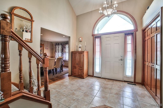 entrance foyer featuring a chandelier, stairs, light tile patterned floors, high vaulted ceiling, and baseboards