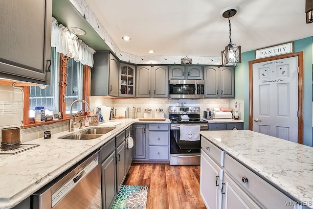 kitchen with appliances with stainless steel finishes, a sink, gray cabinets, backsplash, and light wood-type flooring