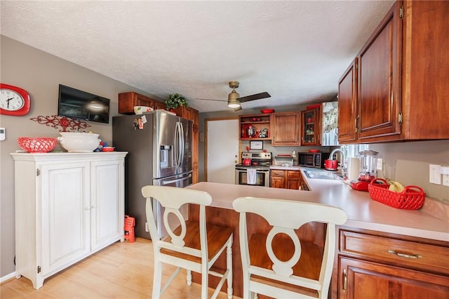 kitchen with stainless steel appliances, a sink, light countertops, a peninsula, and light wood-type flooring