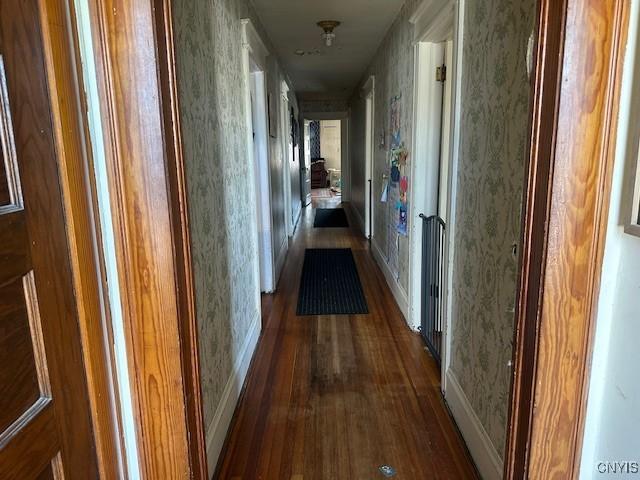 hallway with dark wood-style floors, wallpapered walls, and baseboards