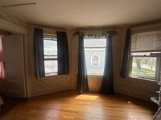 unfurnished room featuring light wood-style floors, wallpapered walls, and baseboards