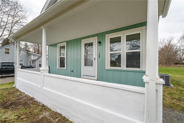 view of exterior entry with cooling unit, fence, covered porch, and board and batten siding