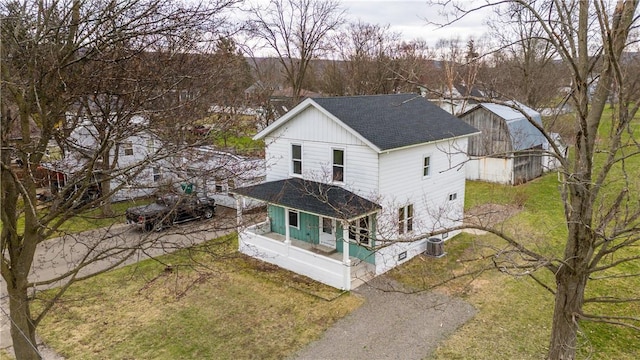 view of front of home with roof with shingles, covered porch, a front lawn, and central AC
