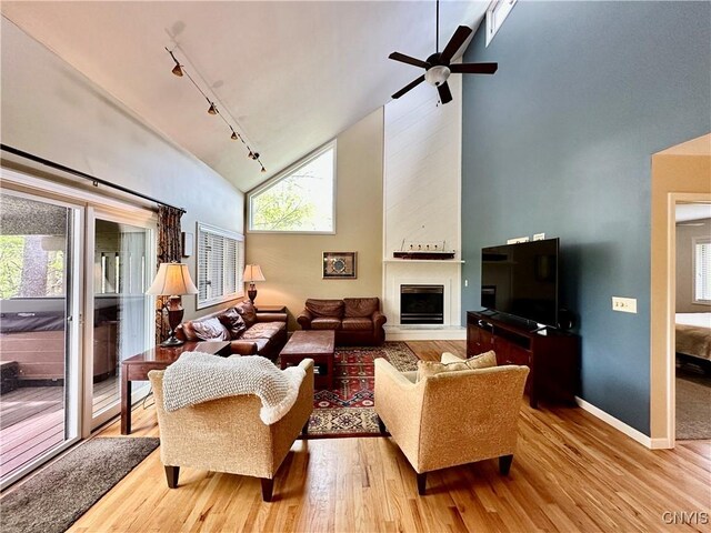 living area featuring high vaulted ceiling, track lighting, wood finished floors, a fireplace, and baseboards