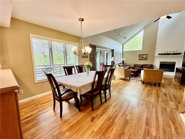 dining room with light wood-style flooring, a chandelier, a fireplace, baseboards, and high vaulted ceiling
