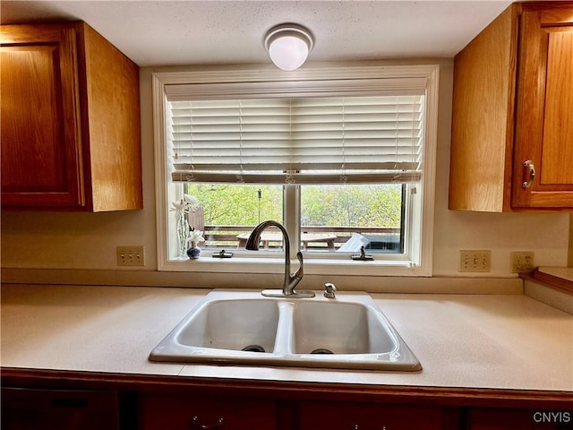 kitchen featuring a sink, light countertops, plenty of natural light, and brown cabinets