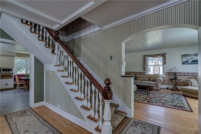stairway with wood finished floors, healthy amount of natural light, baseboards, arched walkways, and ornamental molding