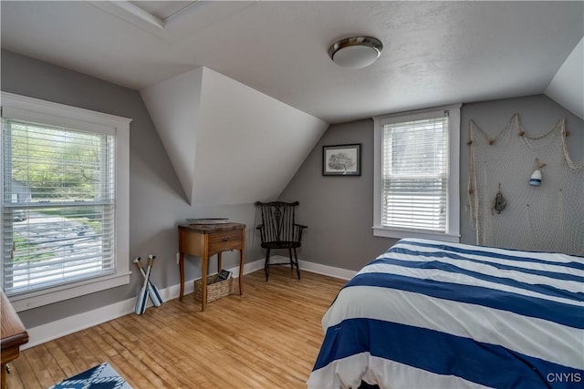 bedroom featuring light wood-style floors, multiple windows, lofted ceiling, and baseboards