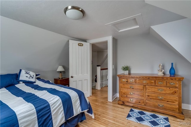 bedroom with attic access, vaulted ceiling, and light wood-type flooring