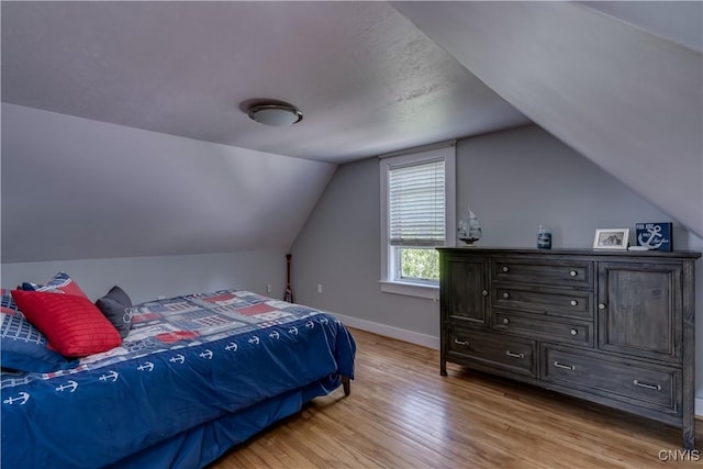 bedroom featuring light wood-type flooring, vaulted ceiling, and baseboards