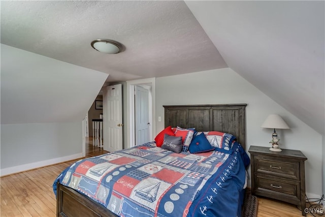 bedroom with light wood-type flooring, vaulted ceiling, baseboards, and a textured ceiling