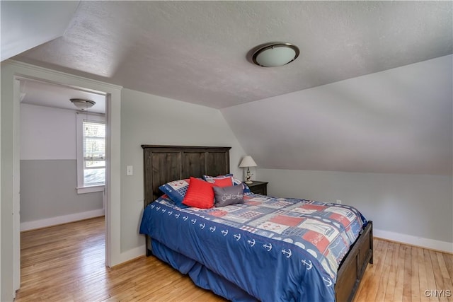 bedroom with light wood-style flooring, baseboards, vaulted ceiling, and a textured ceiling