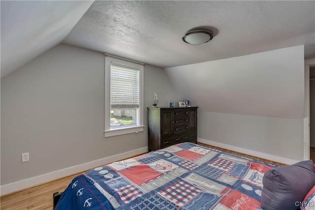 bedroom featuring vaulted ceiling, baseboards, a textured ceiling, and wood finished floors