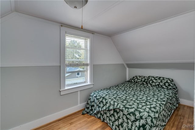 bedroom with vaulted ceiling, wood finished floors, and baseboards