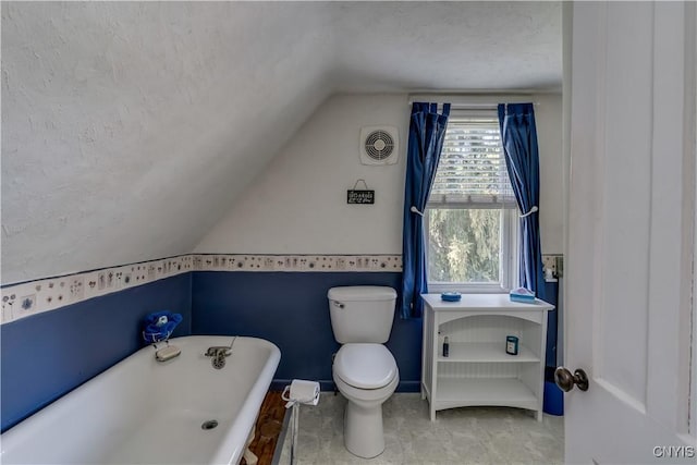 bathroom featuring lofted ceiling, a freestanding bath, toilet, and a textured ceiling