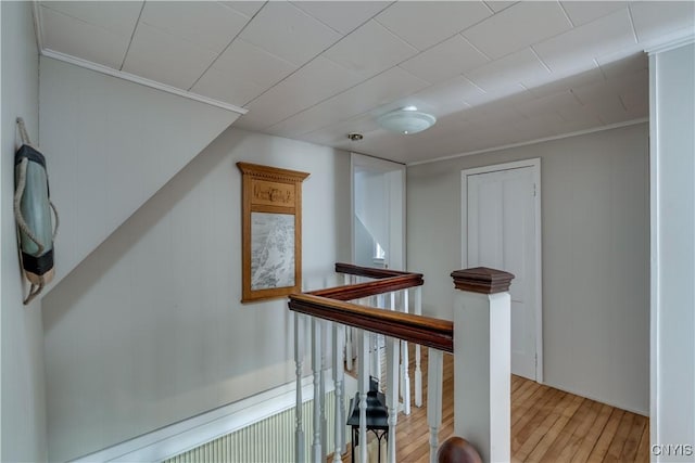 corridor with an upstairs landing, wood finished floors, and ornamental molding