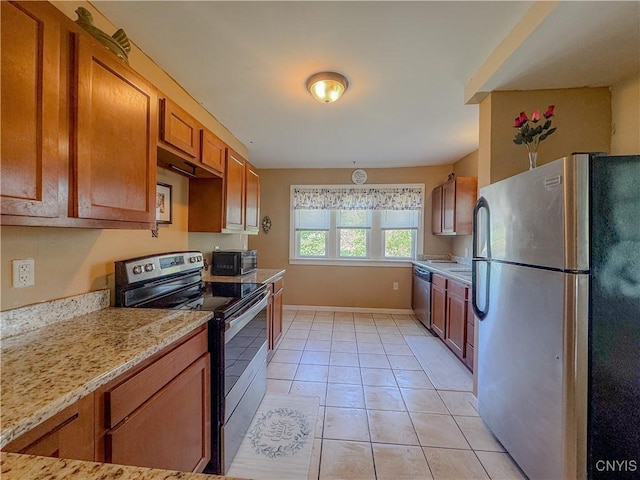 kitchen featuring stainless steel appliances, brown cabinets, light tile patterned flooring, light stone counters, and baseboards