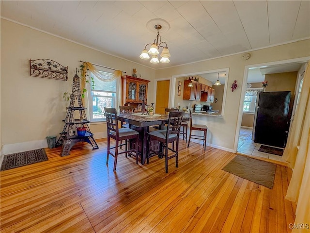 dining room featuring a chandelier, healthy amount of natural light, light wood finished floors, ornamental molding, and baseboards