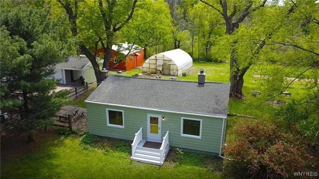 back of property with an outbuilding, a yard, an exterior structure, a chimney, and a shingled roof