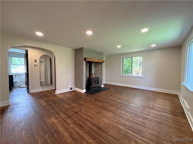 unfurnished living room featuring dark wood-type flooring, baseboards, arched walkways, a wood stove, and recessed lighting
