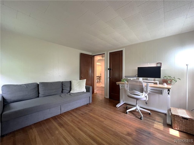 home office featuring wood finished floors, arched walkways, and a decorative wall