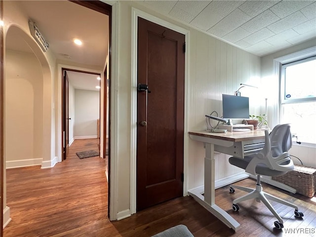 office area with wood finished floors, arched walkways, healthy amount of natural light, and baseboards