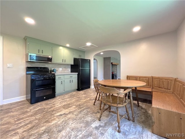 kitchen featuring black appliances, green cabinetry, arched walkways, tasteful backsplash, and baseboards