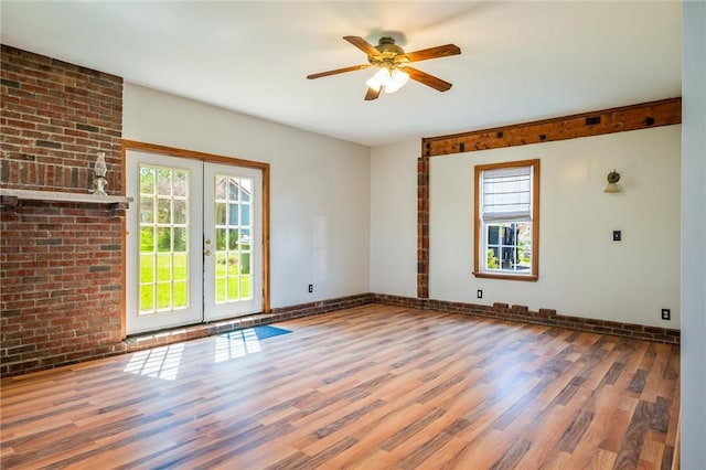 spare room featuring plenty of natural light, wood finished floors, french doors, a ceiling fan, and brick wall