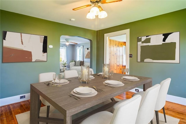 dining space featuring a ceiling fan, arched walkways, baseboards, and wood finished floors