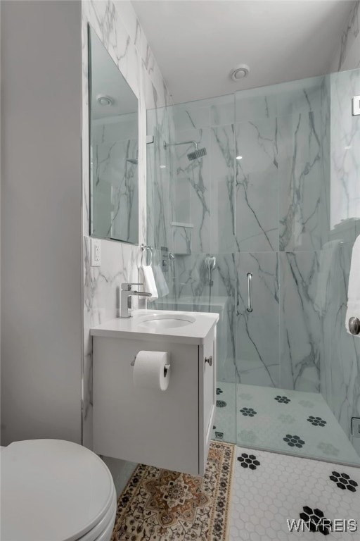 full bath featuring a marble finish shower, vanity, toilet, and tile walls
