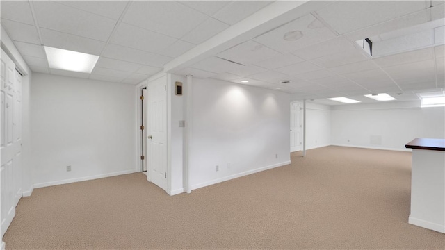 below grade area featuring light carpet, a paneled ceiling, and baseboards