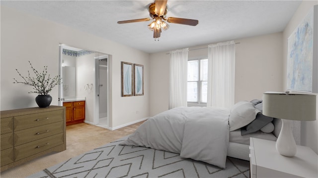 bedroom with light carpet, baseboards, a textured ceiling, ensuite bathroom, and ceiling fan