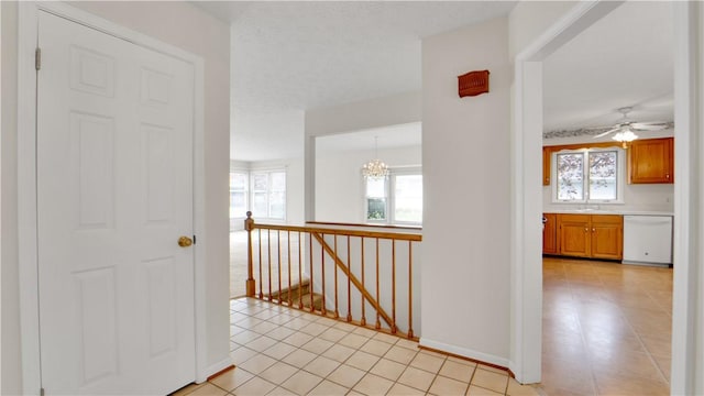 hall featuring an upstairs landing, a chandelier, light tile patterned flooring, baseboards, and a sink