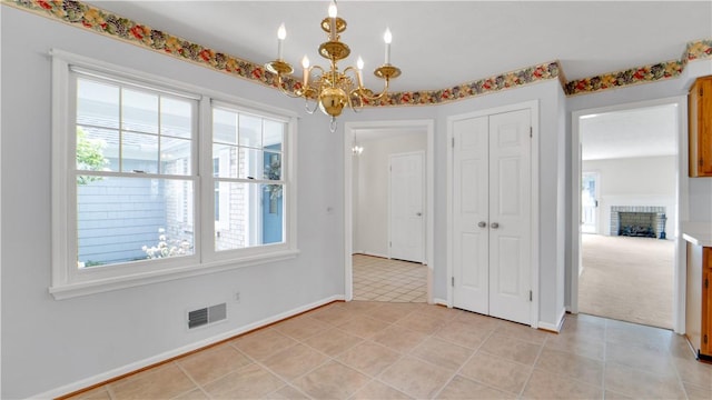 unfurnished dining area with a chandelier, healthy amount of natural light, baseboards, and a brick fireplace