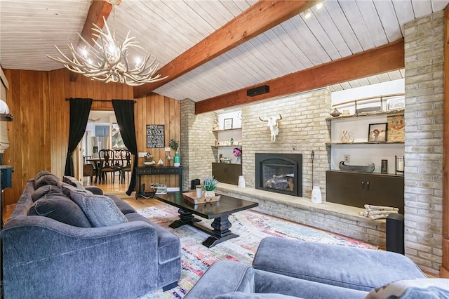 living area with a chandelier, a brick fireplace, beam ceiling, wooden walls, and wood finished floors